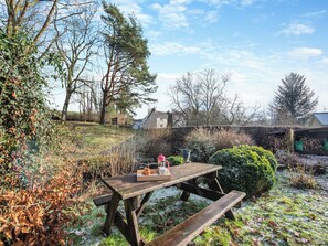 Een picknicktafel met een schaal eten en een drankje, omringd door bomen en een stenen muur.