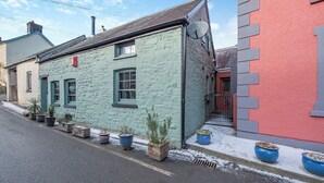 Een smalle straat met een rij potplanten langs de stoep, een gebouw met een schuin dak en een schotelantenne aan de zijkant.
