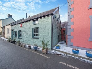 Een smalle straat met een rij potplanten langs de stoep, een gebouw met een schuin dak en een schotelantenne aan de zijkant.