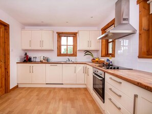 A modern kitchen with white cabinets, a wooden countertop, a stainless steel range hood, and a window with a view.
