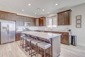 A modern kitchen with a large island, bar stools, stainless steel appliances, and wooden cabinets. - The Turtle Cove- Unobstructed vibrant sunset views (Washington)