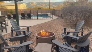 An outdoor seating area with Adirondack chairs, a fire pit, and a pool in the background.