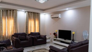 Uma sala de estar com sofás de couro, uma televisão de tela plana, um móvel de entretenimento branco e um vaso decorativo.