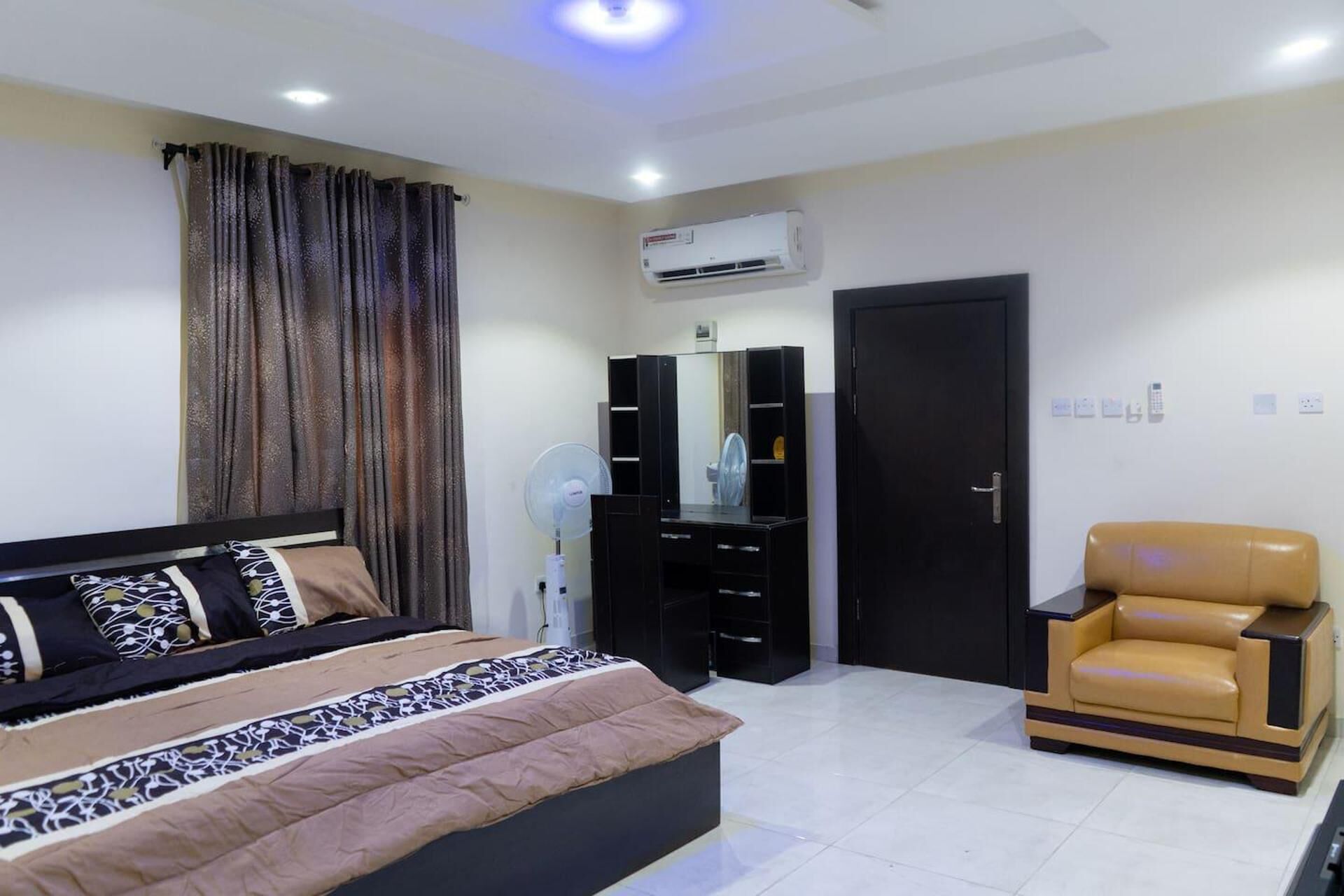 A bedroom with a bed, a wardrobe, a mirror, a chair, and an air conditioning unit.