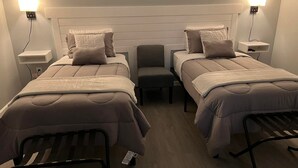 A hotel room with two beds, a chair, and bedside lamps. - The Crossroad Inn (Lineville)