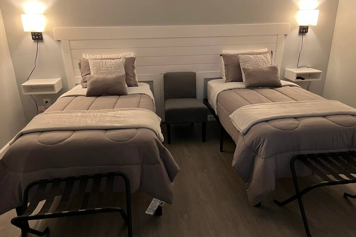 A hotel room with two beds, a chair, and bedside lamps.