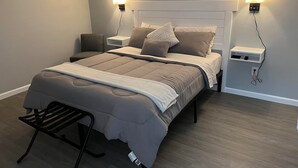 A neatly made bed with a headboard, two bedside tables, and a bench at the foot of the bed. - The Crossroad Inn (Lineville)