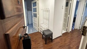 Ein Flur mit einer Holztür, einer kleinen Bank und einem Metallregal.