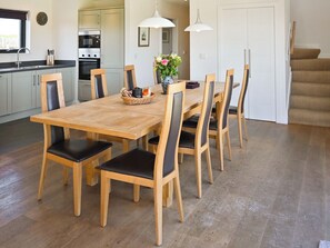 A dining area with a wooden table and chairs, a kitchen in the background, and a staircase leading to another level. - The Longhouse at Threave (Castle Douglas)