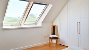 Une chambre avec un plafond en pente, un puits de lumière, un lit recouvert d’une courtepointe colorée, une chaise et une armoire.