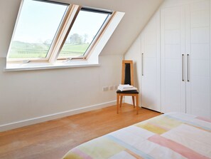 Une chambre avec un plafond en pente, un puits de lumière, un lit recouvert d’une courtepointe colorée, une chaise et une armoire.