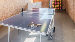 Une table de ping-pong avec deux raquettes et un filet, placée dans une pièce aux murs en bois et ornée d’une décoration murale colorée à motifs de points.