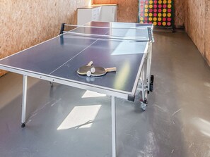 Une table de ping-pong avec deux raquettes et un filet, placée dans une pièce aux murs en bois et ornée d’une décoration murale colorée à motifs de points.