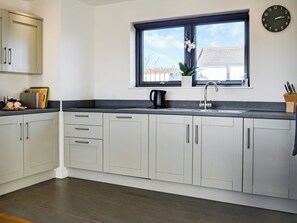 A modern kitchen with white cabinets, a black countertop, a window with a view, and a clock on the wall.