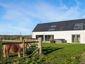 Une maison moderne avec une grande pelouse, un espace clos où se trouve un cheval, et un ciel dégagé.