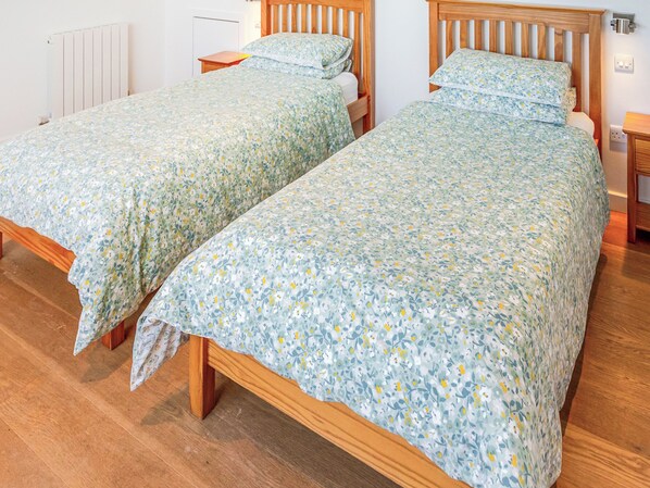 Two single beds with wooden frames and floral bedding in a room with wooden flooring and white walls.