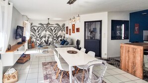 Un espacio habitable moderno con zona de comedor, sofá, televisor y pared estampada.