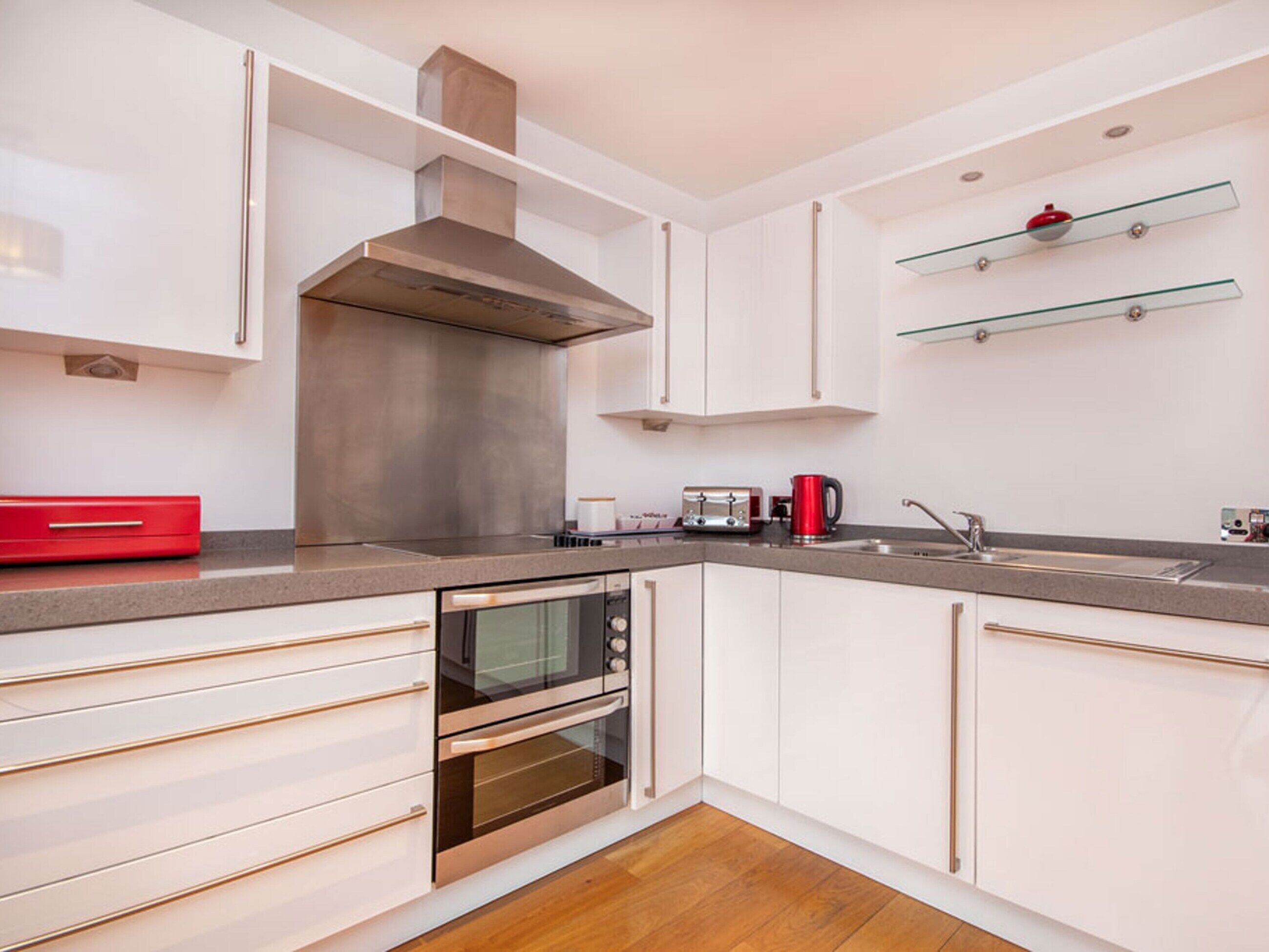 A modern kitchen with white cabinets, stainless steel appliances, and a wooden floor.