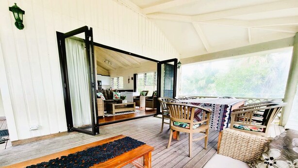 A spacious veranda with a wooden bench, wicker furniture, and a view of the interior. - Natura Turtle Bungalow (Rarotonga)