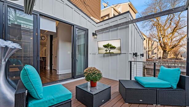 Une terrasse extérieure moderne, avec des meubles en osier, une plante en pot et une œuvre d’art encadrée.