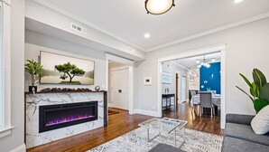 Un salon moderne doté d’une cheminée, d’un coin repas et d’une cuisine visible à travers une porte ouverte.