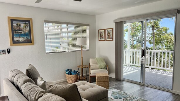 A living room with a beige sofa, a floor lamp, a side table, and a view of the outdoors through a sliding glass door. - Afforable & quaint upstairs 2Bedroom 1Bath apartment with lanai and Ocean views (Kailua-Kona)