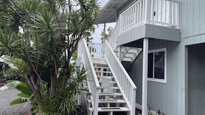 A two-story building with a white exterior, a balcony, and a staircase leading to the upper floor. - Afforable & quaint upstairs 2Bedroom 1Bath apartment with lanai and Ocean views (Kailua-Kona)