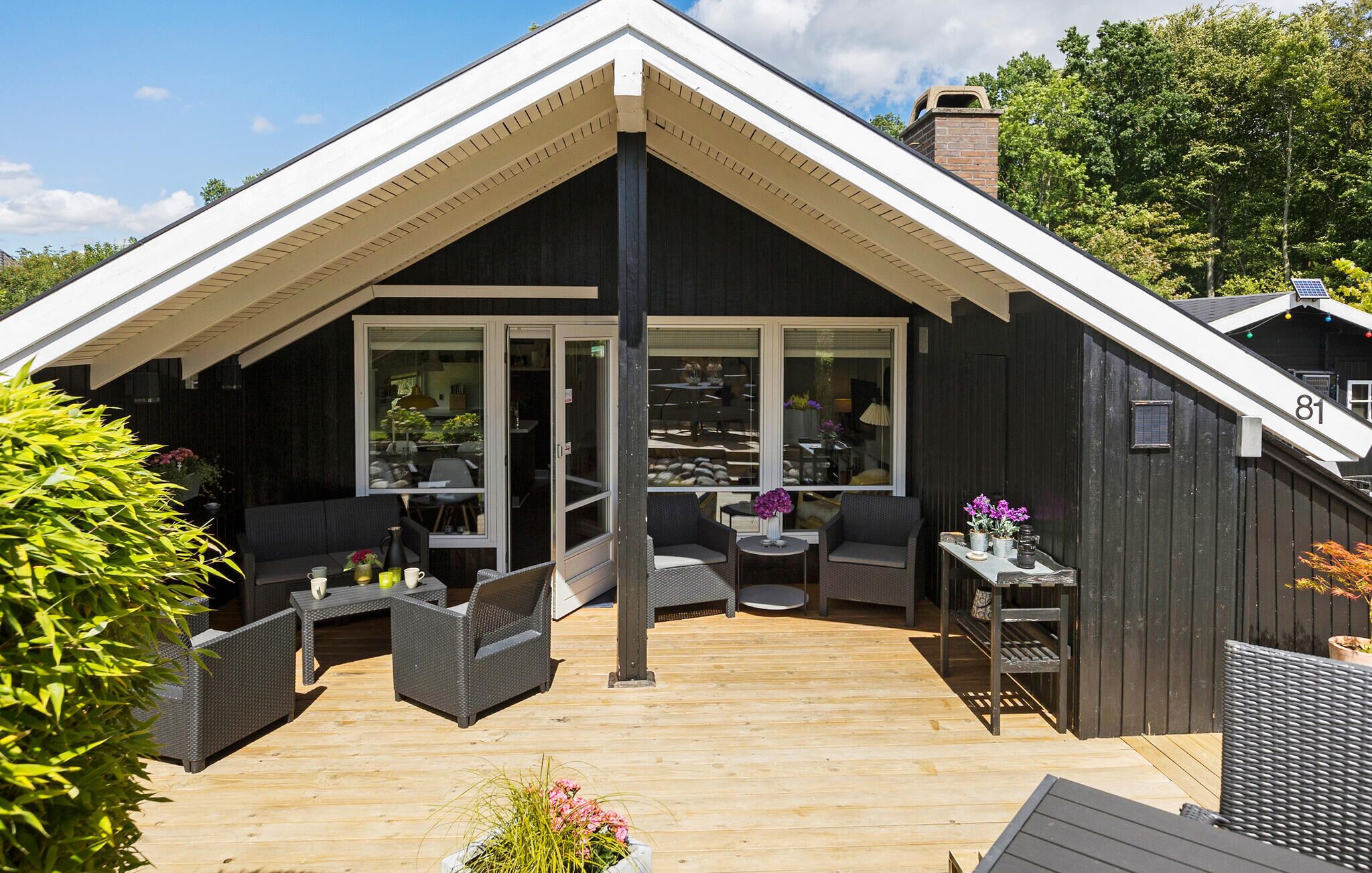 A modern house with a large deck, large windows, and outdoor furniture.