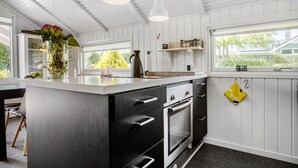 A kitchen with white wooden paneling, a central island with a sink, a stove, and a window with a view of greenery. - Awesome home in Egernsund with kitchen (Egernsund)
