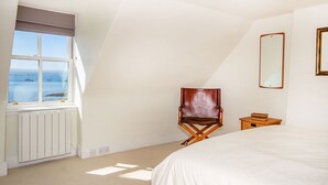 A bedroom with a large bed, a window with a view of the sea, a chair, and a small table. - 2 bedroom accommodation in Fortrose (Fortrose)