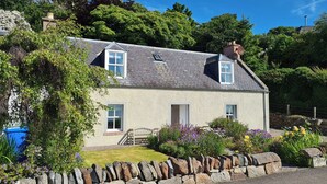 A two-story house with a stone facade, a sloped roof, and a stone wall in front. - 2 bedroom accommodation in Fortrose (Fortrose)