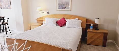 A neatly arranged bedroom with a wooden bed, white bedding, a bedside lamp, and a small table with a tissue box.