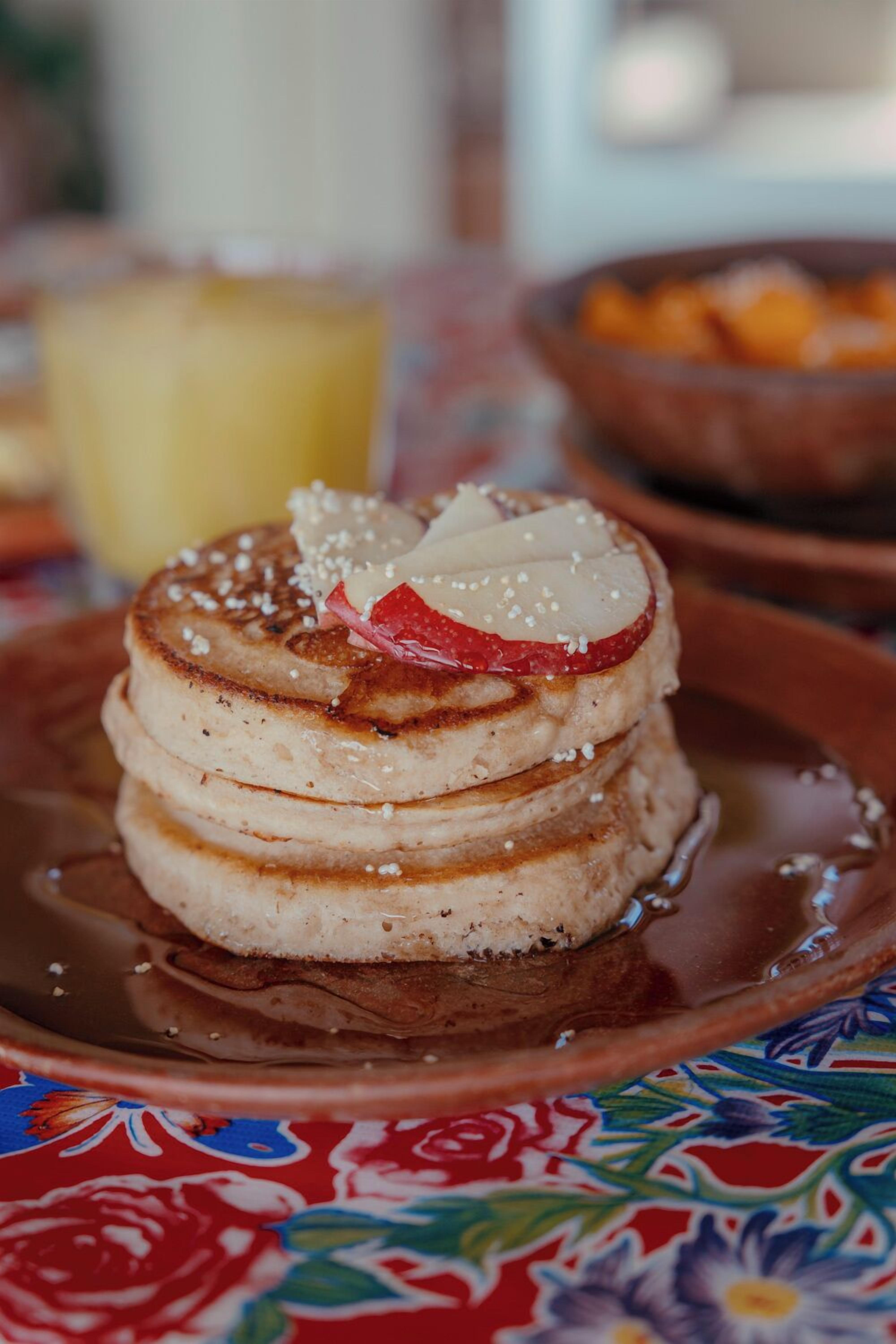 Une pile de crêpes, une tranche de pomme et une pincée de sucre, le tout présenté sur une assiette en céramique.