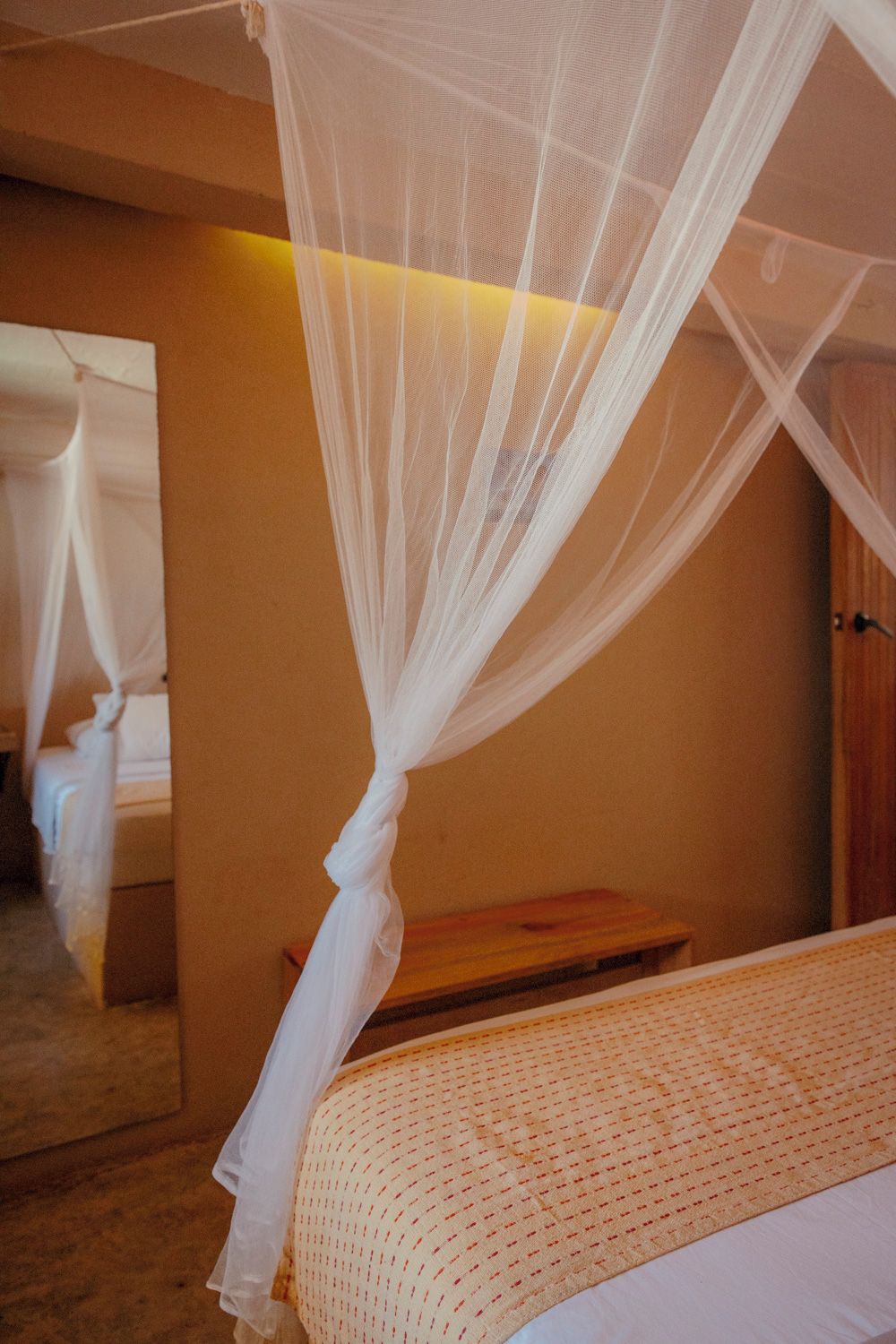 Ein Hotelzimmer mit einem Bett, einem Nachttisch aus Holz, einem Spiegel und einem weißen Baldachin.