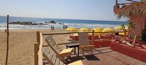 A beachside seating area with wooden chairs and tables, yellow umbrellas, and a view of the ocean.
