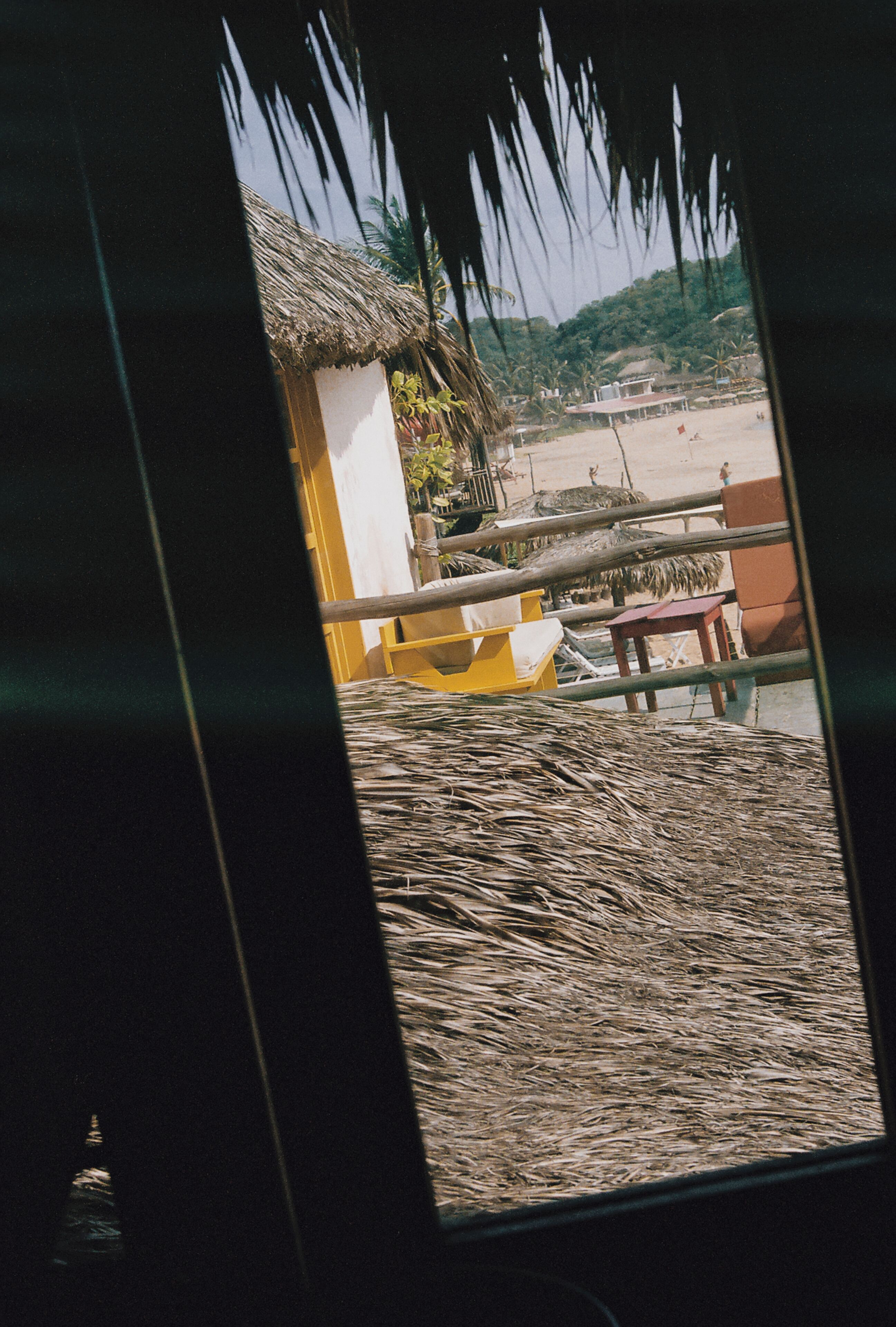 A view from a window with a thatched roof, a yellow chair, and a small table outside.