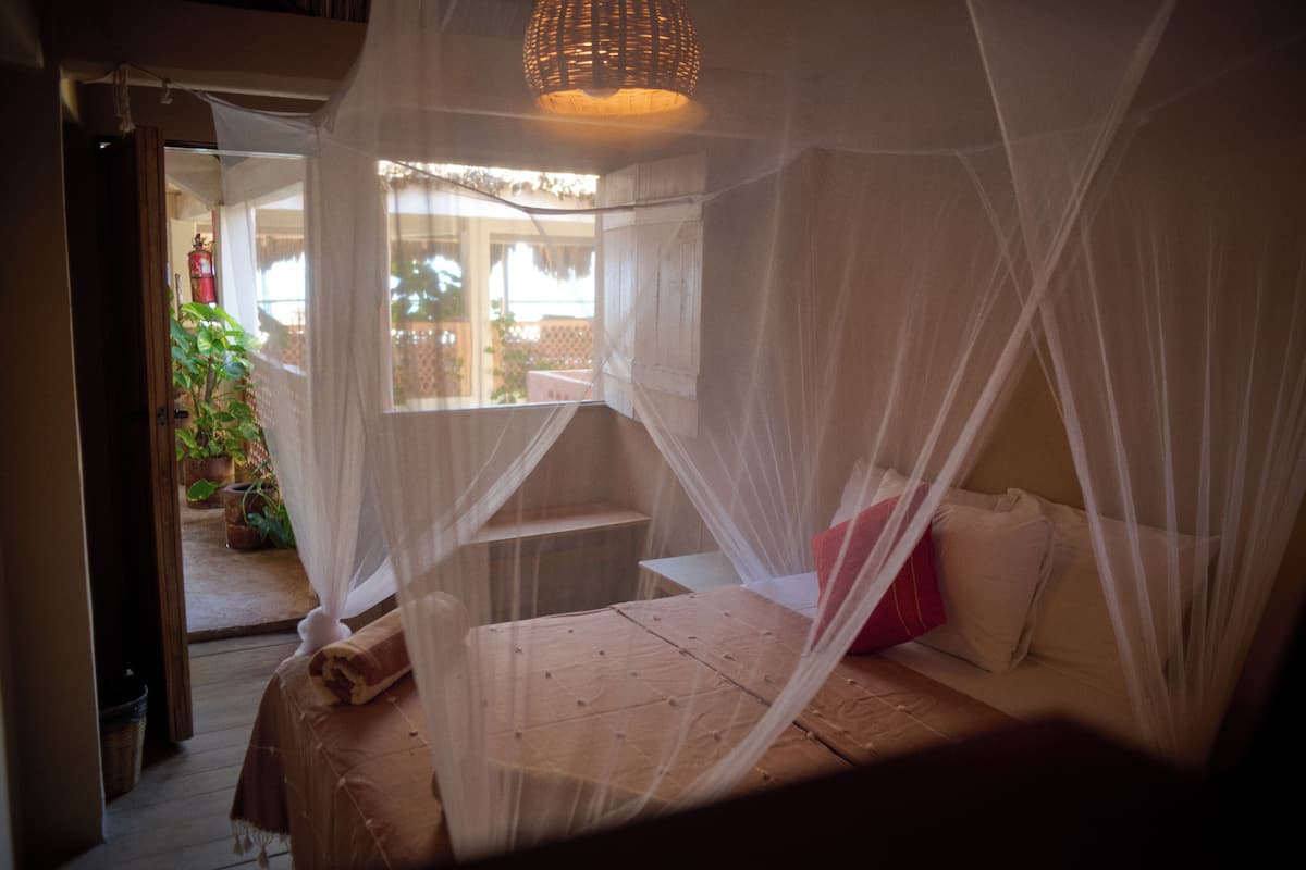 Une chambre à coucher avec un lit à baldaquin, une petite table et une fenêtre donnant sur un jardin.