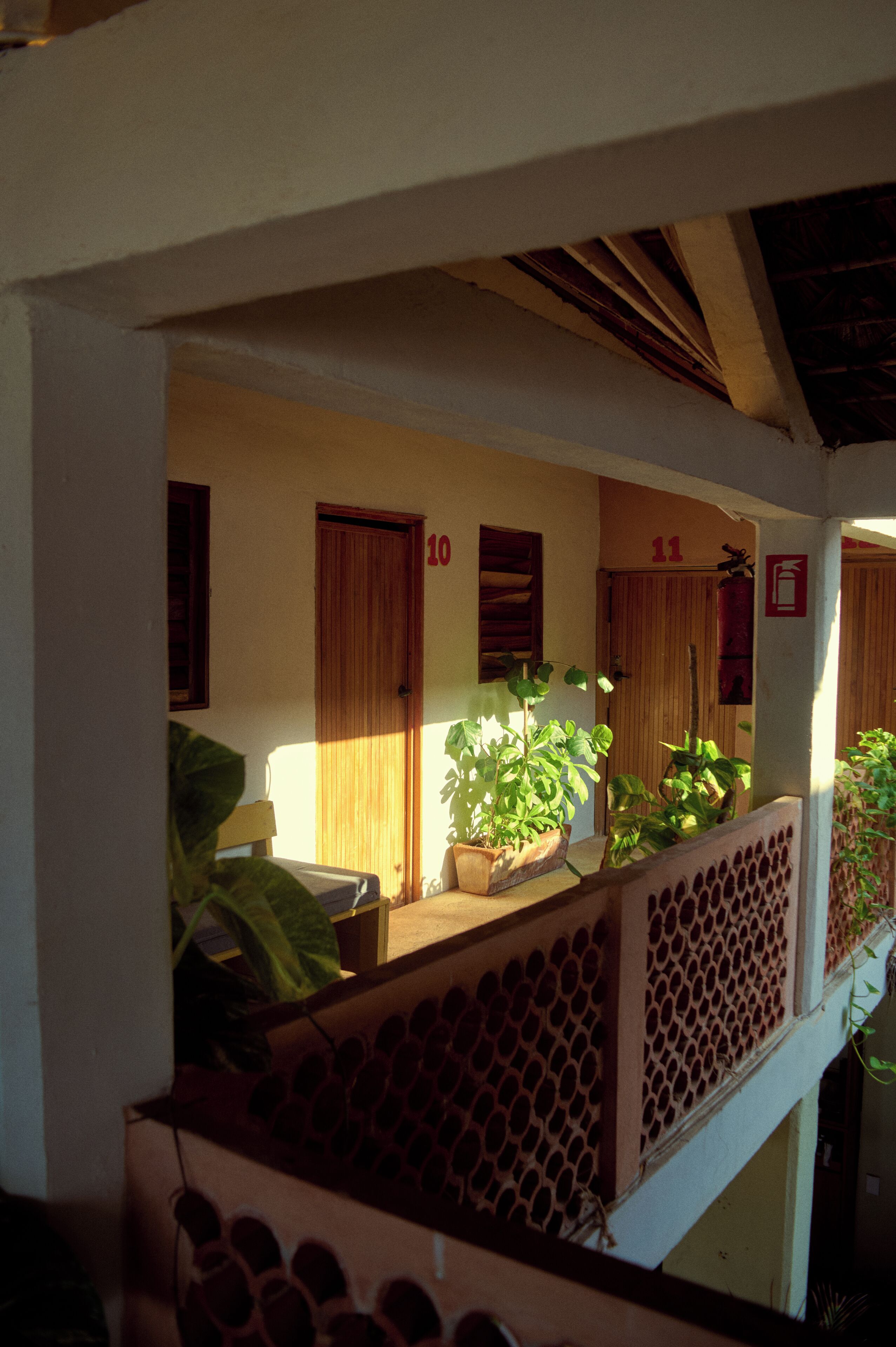 A hotel corridor with doors numbered 10 and 11, potted plants, and a balcony with a lattice railing.