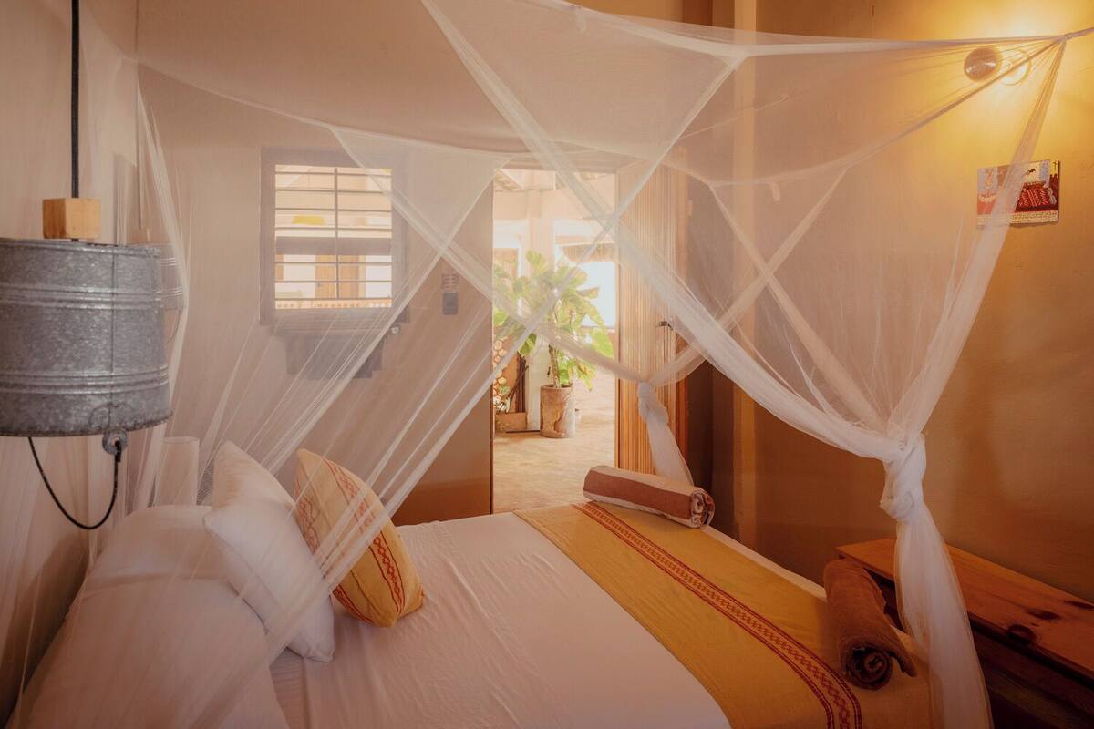 Une chambre avec un lit, une moustiquaire, une lampe et une fenêtre.