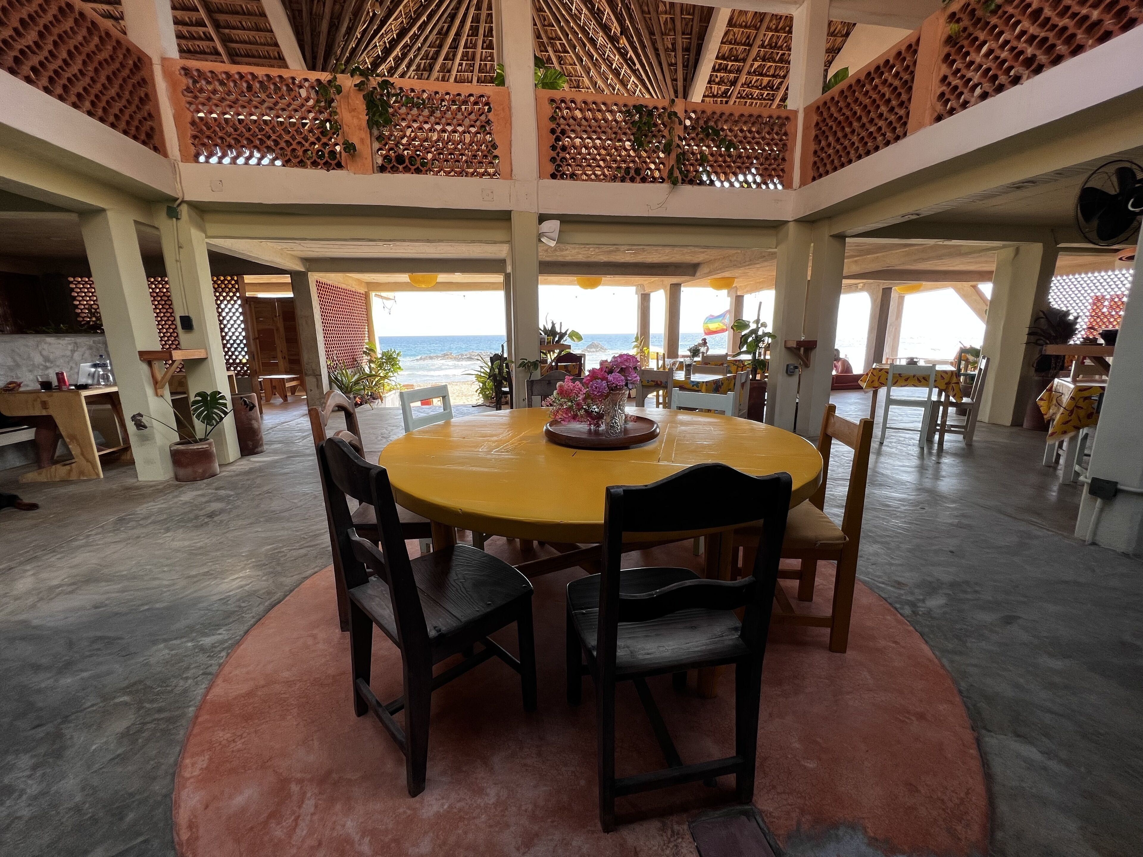 A spacious dining area with a round table and chairs, a view of the beach, and a ceiling with a lattice design.