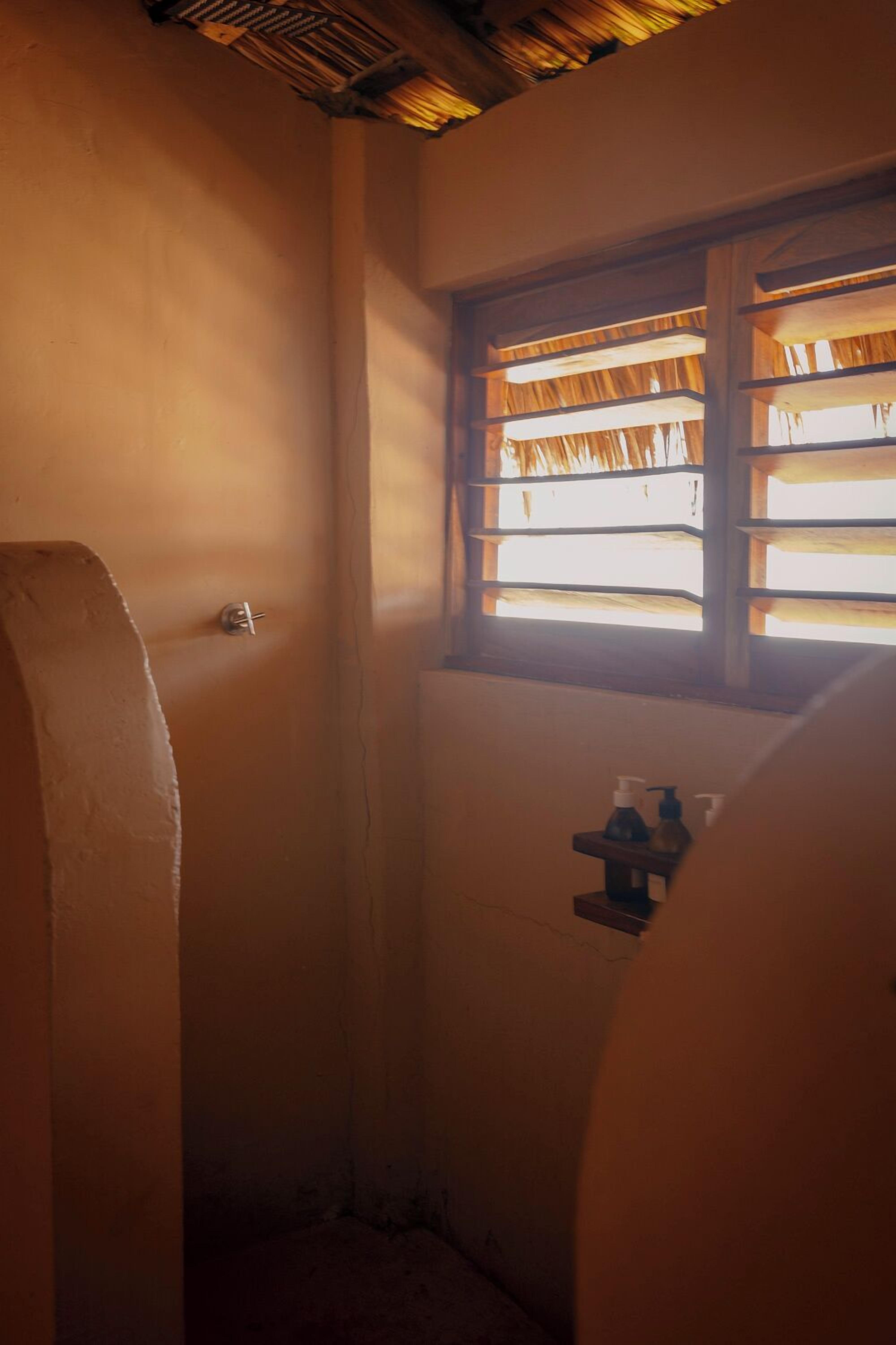 A narrow bathroom with a window, a towel rack, and a small shelf with toiletries.