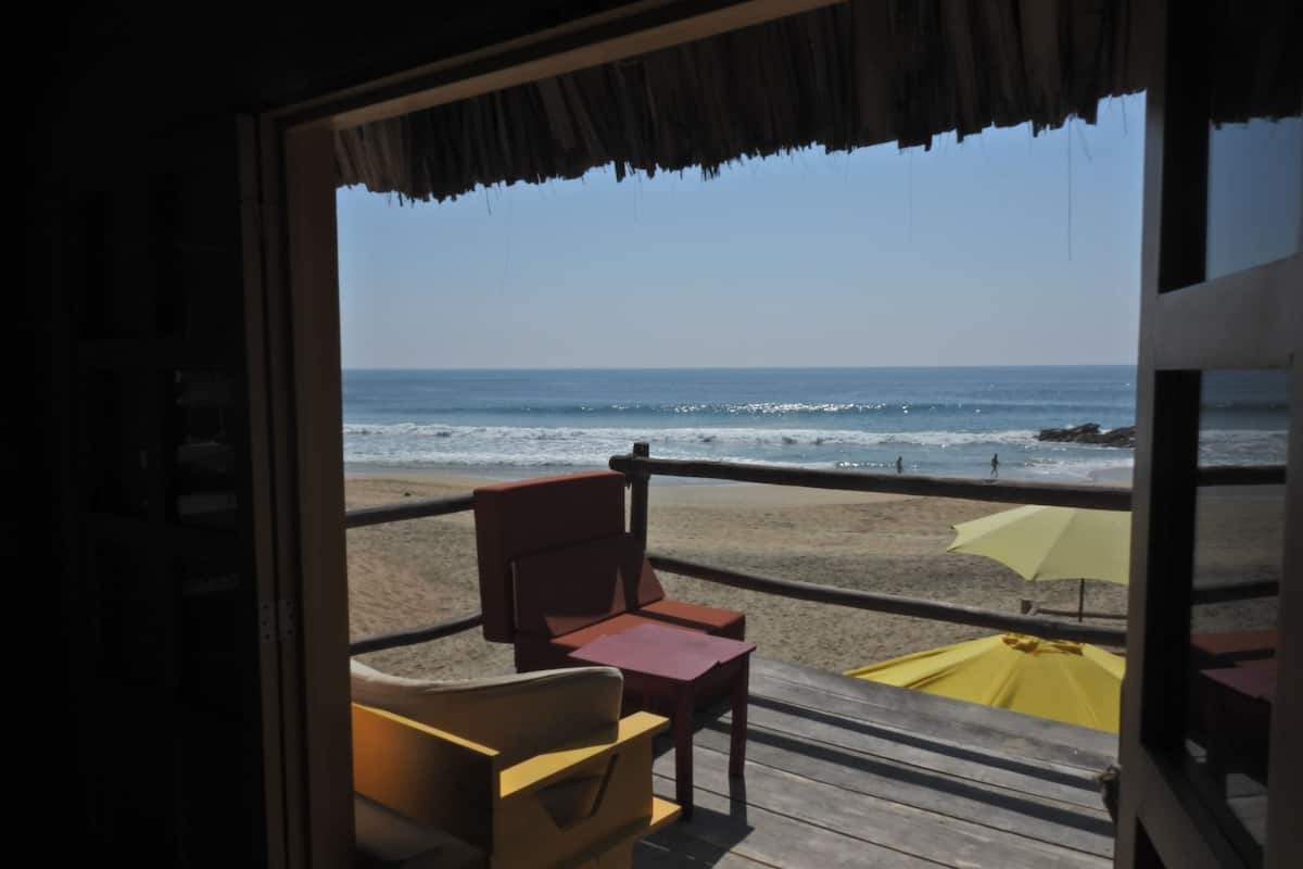 Une vue sur la plage depuis un balcon, avec des chaises en bois et un parasol jaune.