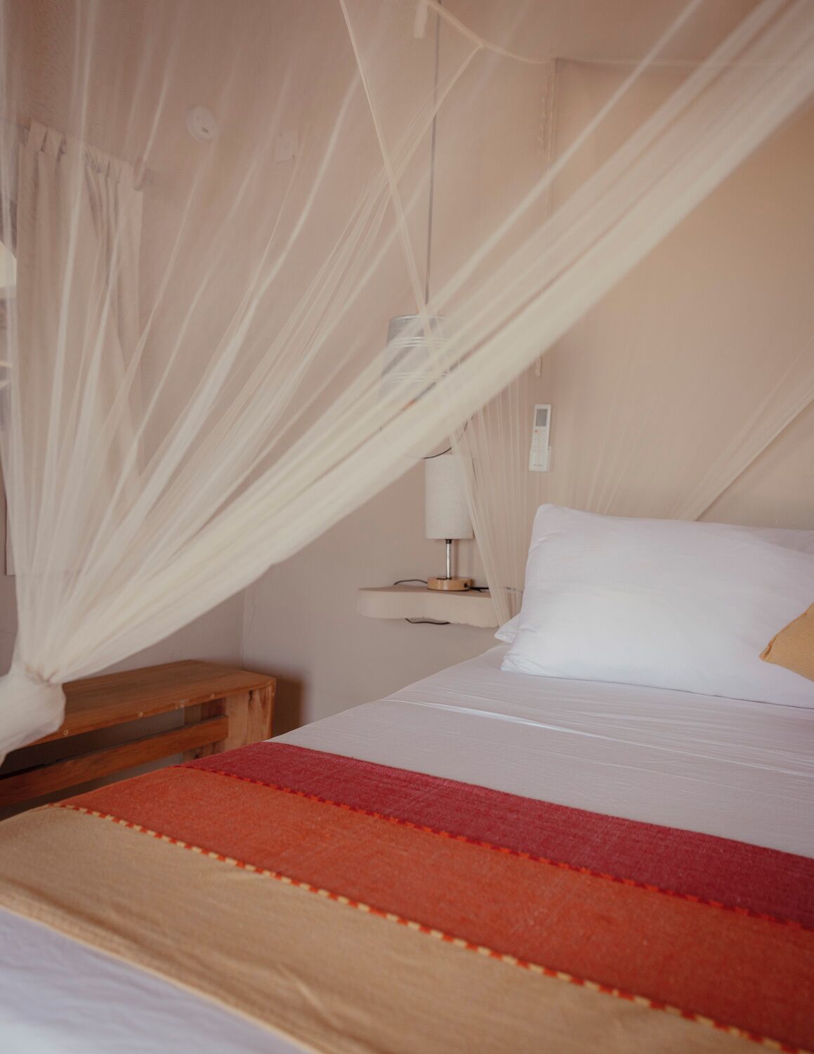 Una cama con dosel blanco, una mesita de noche y una lámpara.