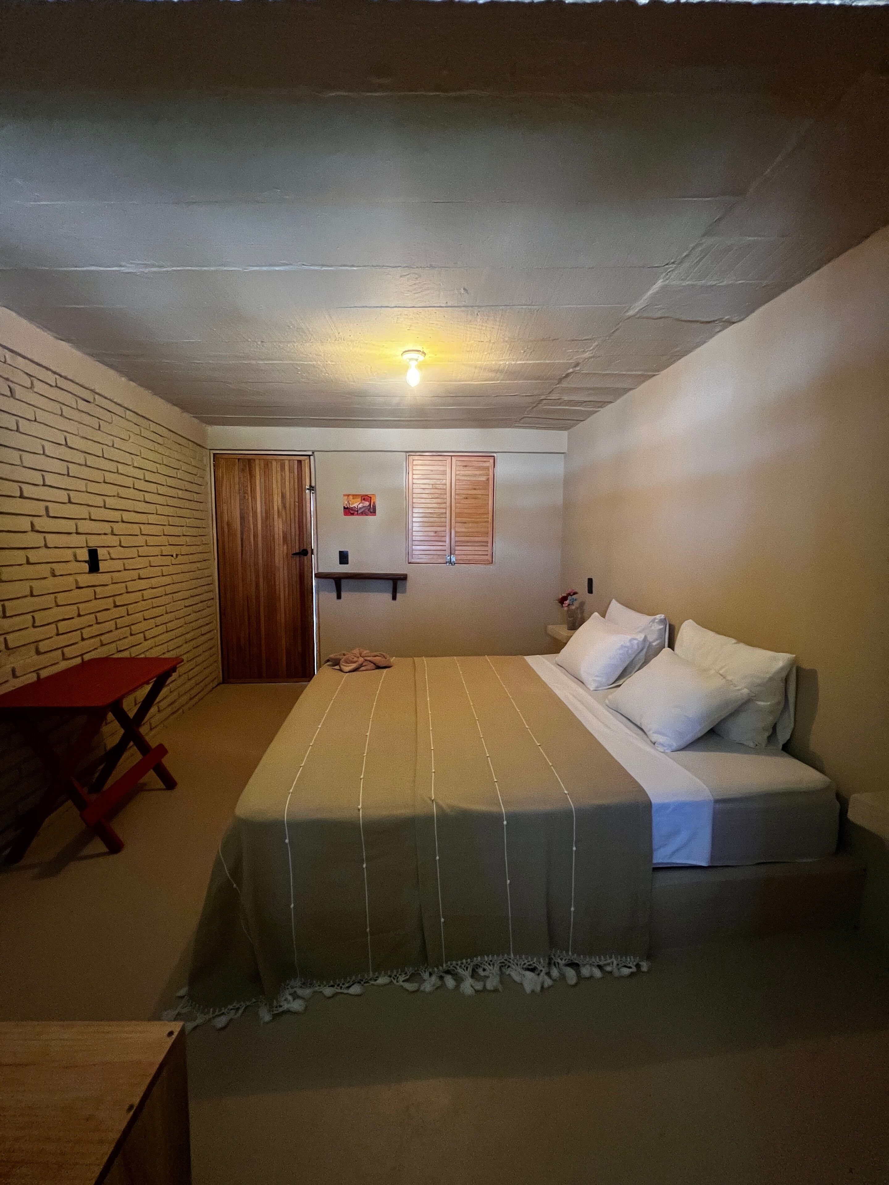 Una habitación con una cama, una mesita, un banco y una puerta de madera.