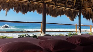 Un salon de plage doté d’un toit de chaume et offrant une vue sur l’océan.