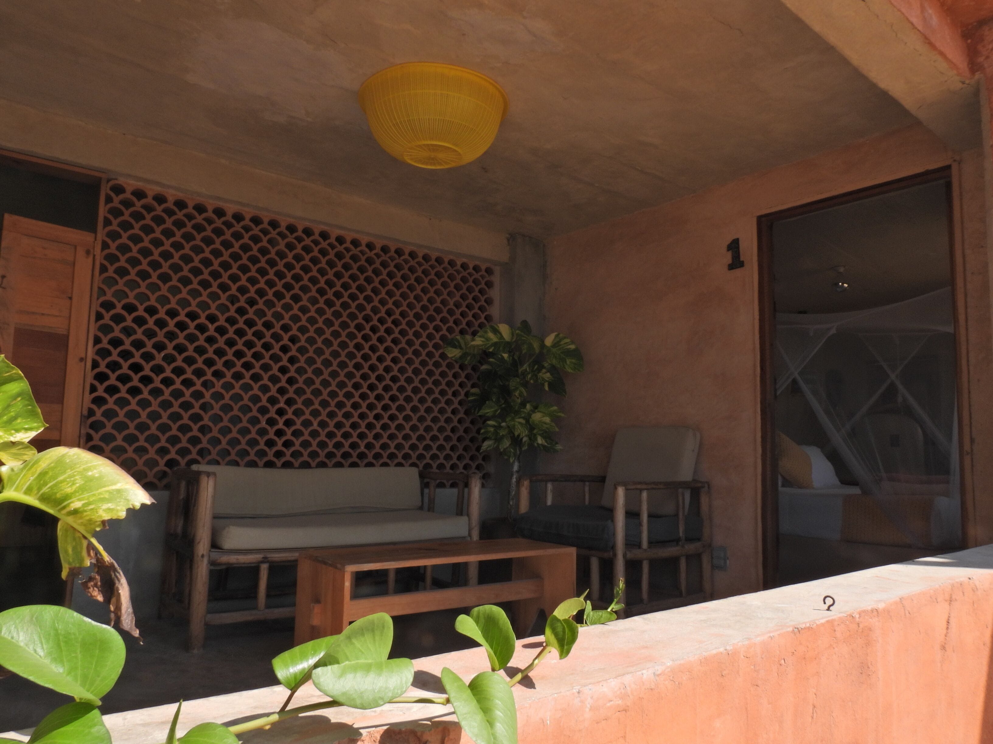 A room with a wooden bench, a small table, a potted plant, and a yellow hanging light fixture.