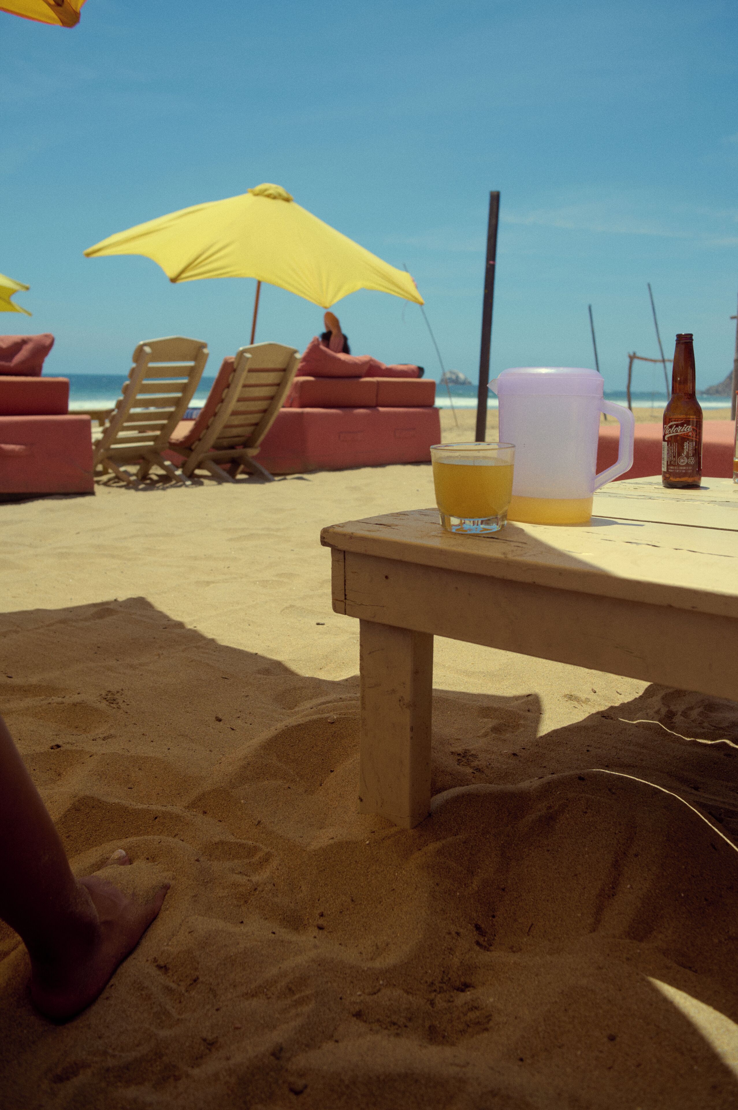 A beach setting with a table, a yellow umbrella, and beach chairs.