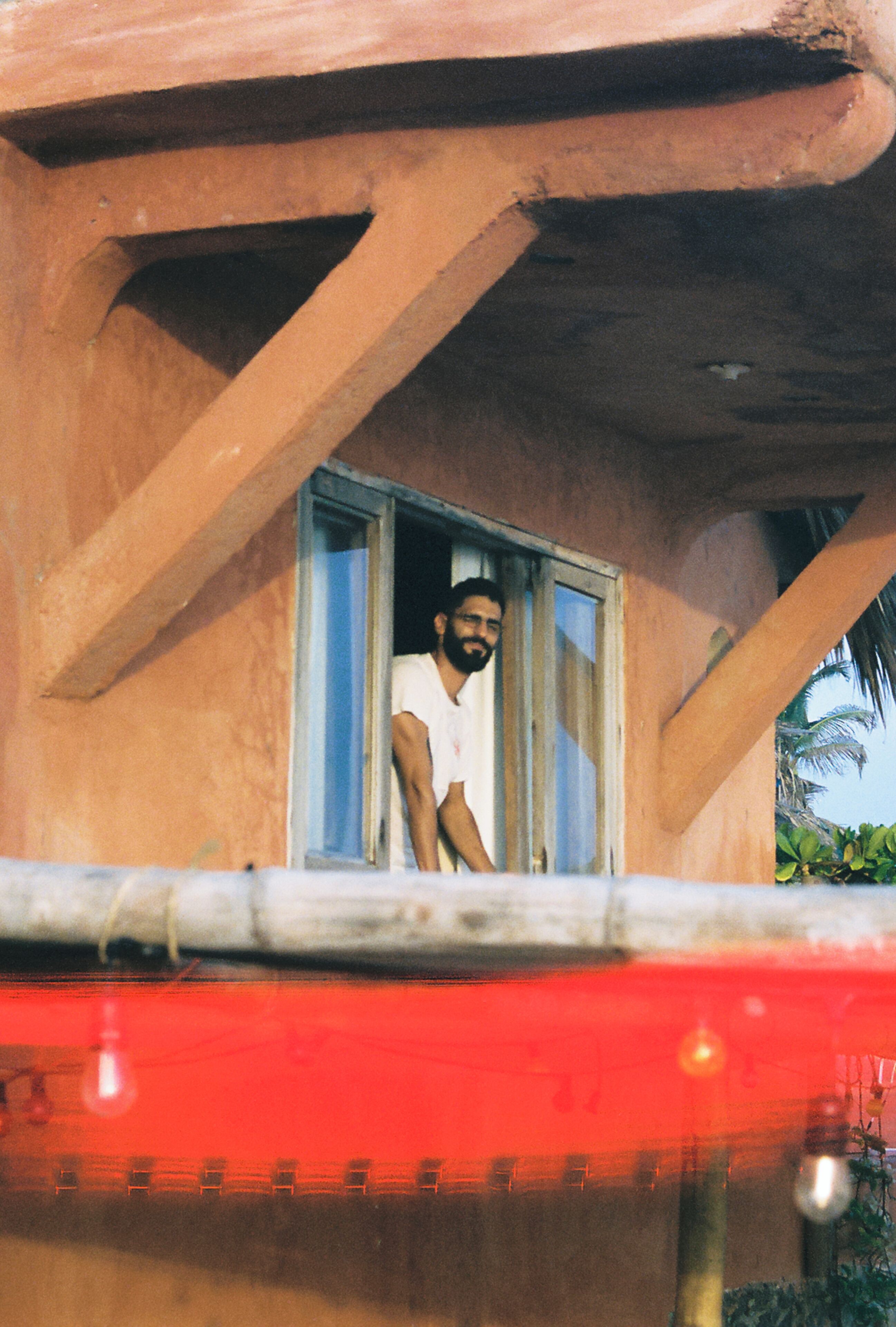 Una persona está de pie junto a una ventana, con vista a un vehículo rojo abajo.