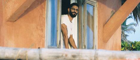 Una persona está de pie junto a una ventana, con vista a un vehículo rojo abajo.