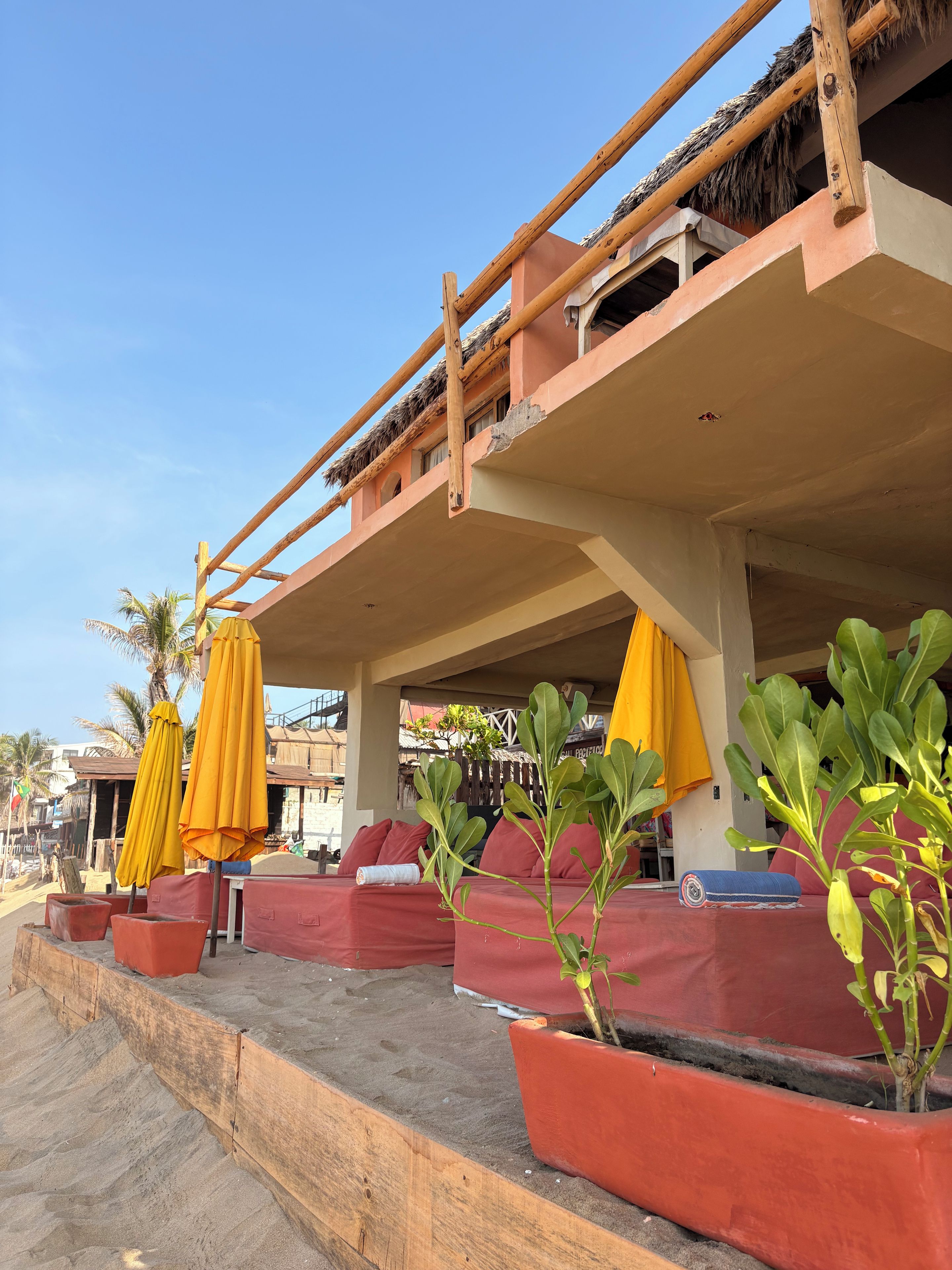 A beachfront seating area with red cushioned benches and yellow umbrellas.